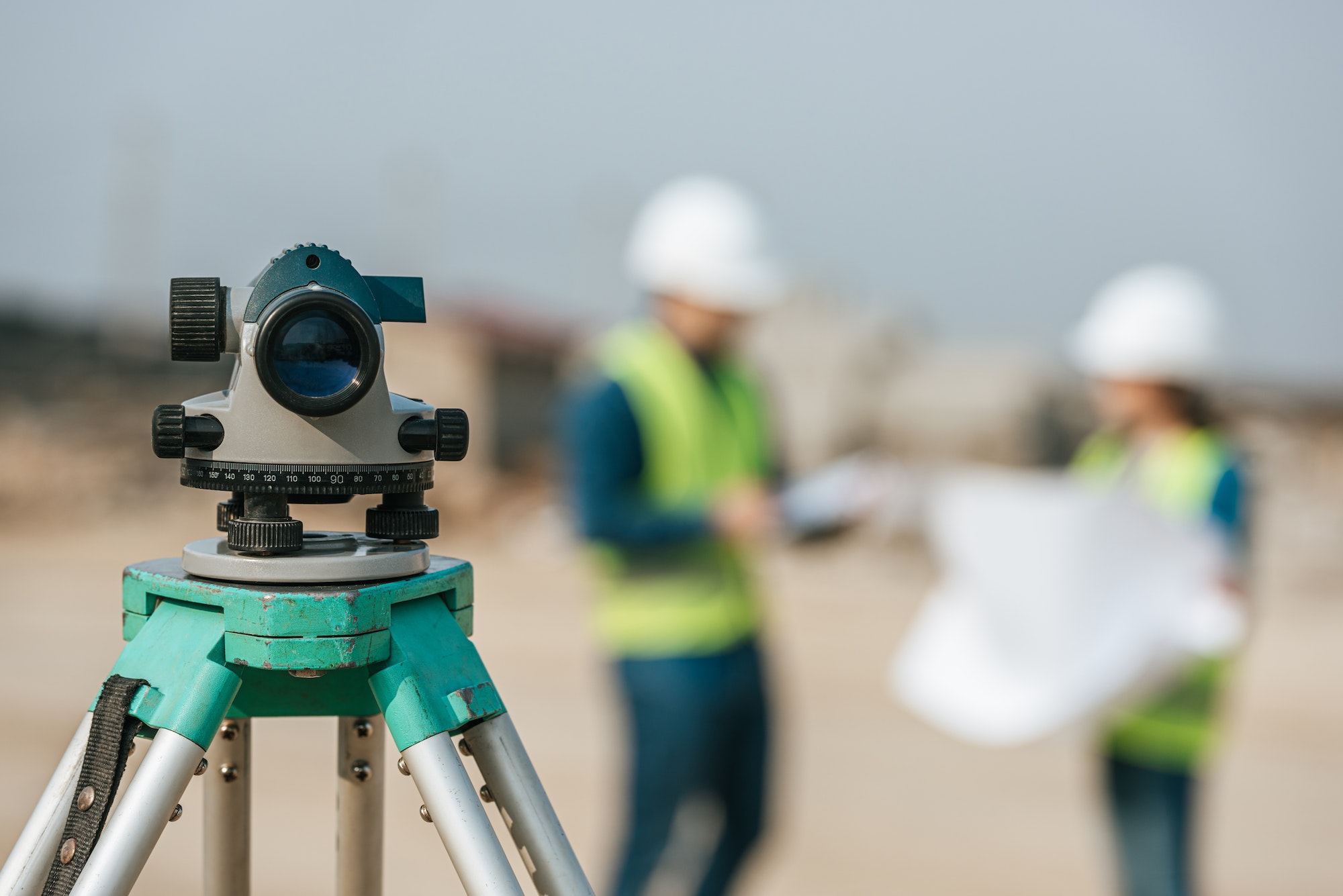 Selective focus of digital level and surveyors with blueprint at background