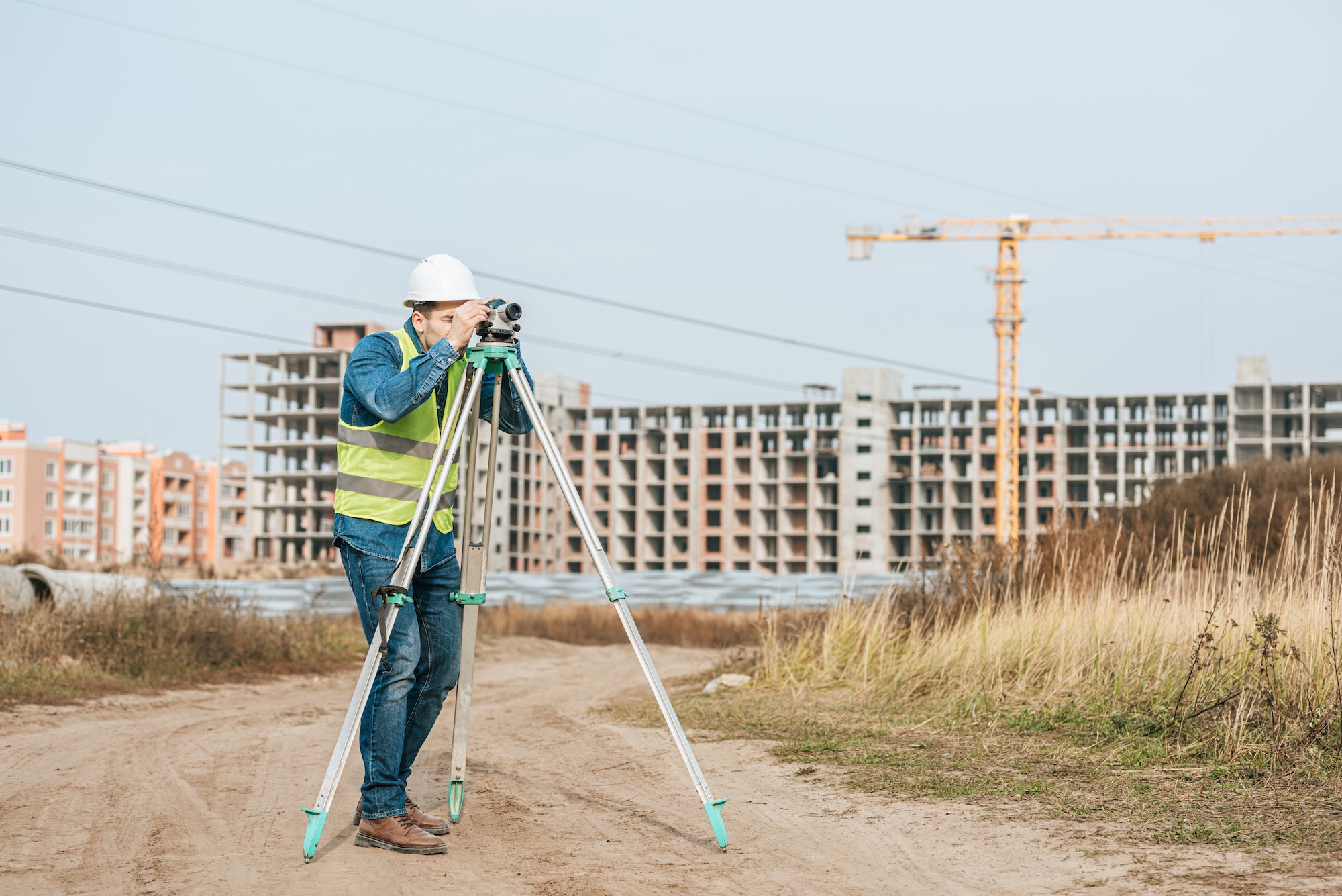 Surveyor looking through digital level on dirt road of construction site